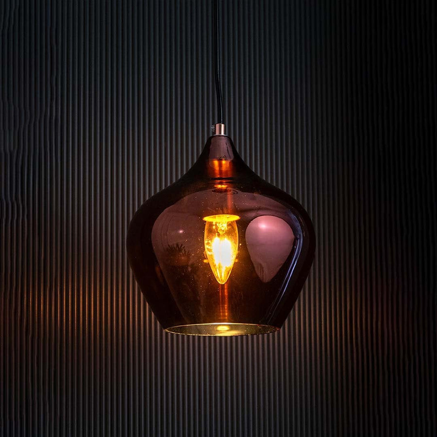 An amber glass pendant light with the bulb turned on against a black background showcasing its warm glow and sleek reflective glass texture.