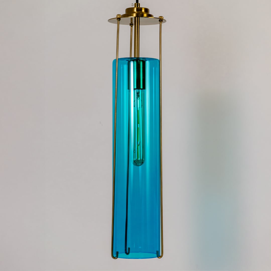Closeup view of the blue glass pendant light showcasing its glossy finish inner tube bulb and polished brass frame with modern detailing.