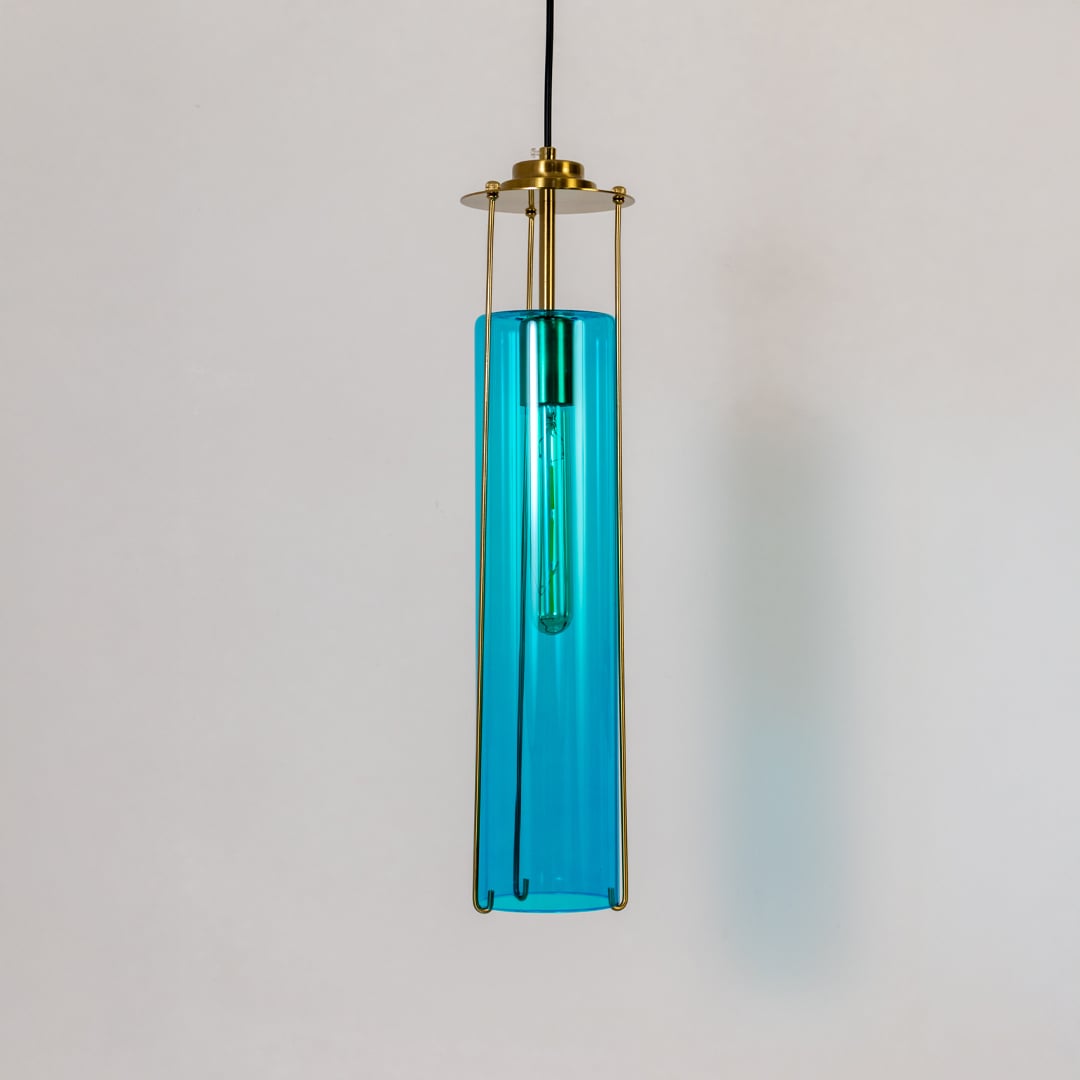 Blue glass pendant light turned off against a crisp white background highlighting its rich color clean lines and modern brass frame design.