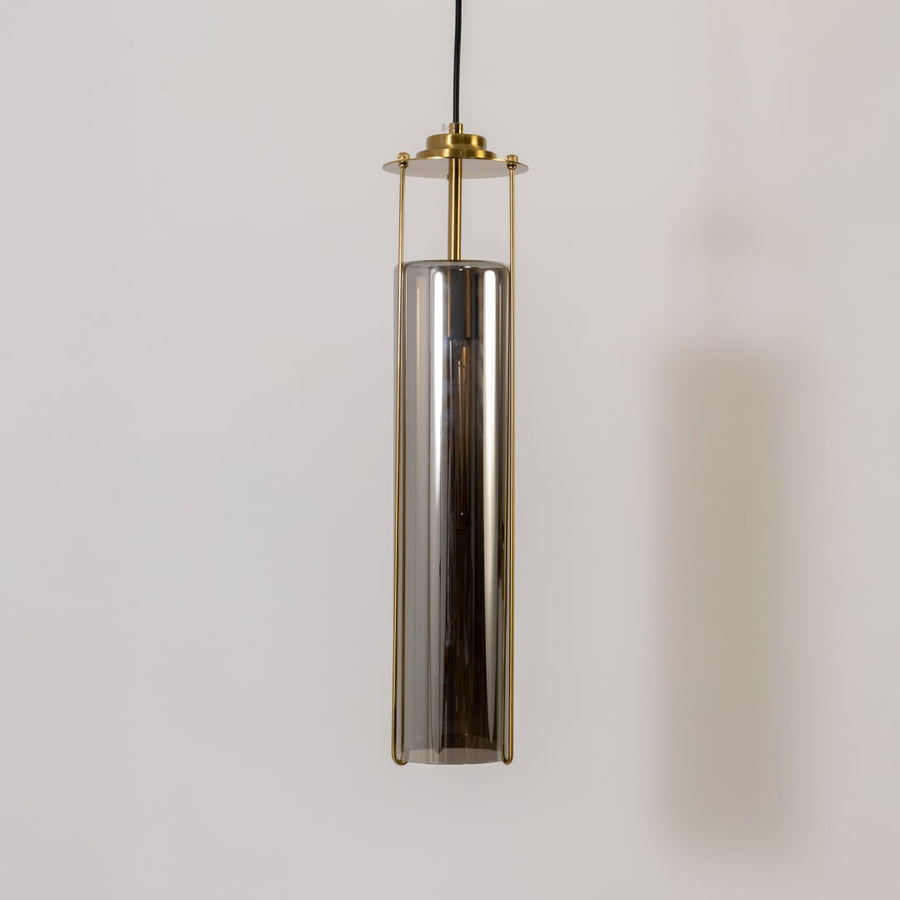 Smoked glass pendant light turned off on a white background showing its tall cylinder shade and refined brass structure in detail.