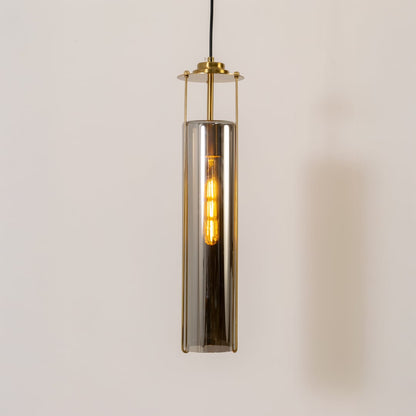 Sleek smoked glass pendant light glowing warmly against a clean white background featuring a tall cylindrical shade and brass frame.