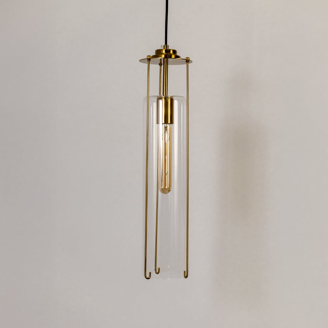 Clear glass pendant light turned off against a white background emphasizing its minimalist cylindrical design and polished brass structure.