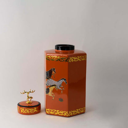 Glossy orange ceramic jar with gold embellishments and artistic motifs perfect for tabletops and elegant living room displays.