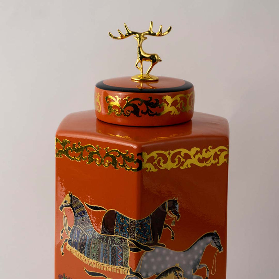 Closeup of orange ceramic jar highlighting the detailed golden border and intricately painted horses for luxurious appeal