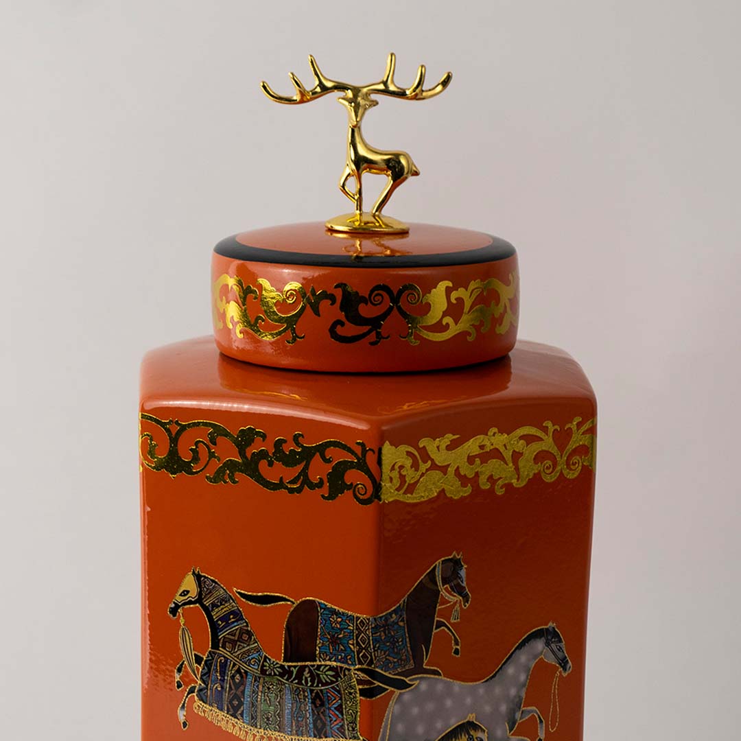 Detailed view of orange ceramic jar showing intricate gold horse artwork and glossy finish with elegant lid topper.