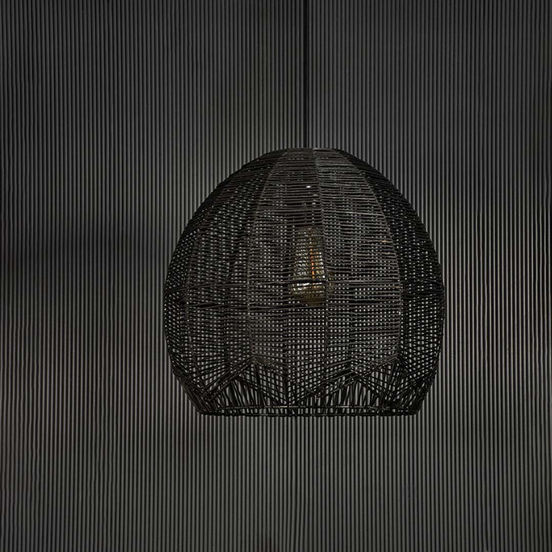 Stylish black rattan pendant light against black background highlighting fine weaving structure and artisanal handmade texture.