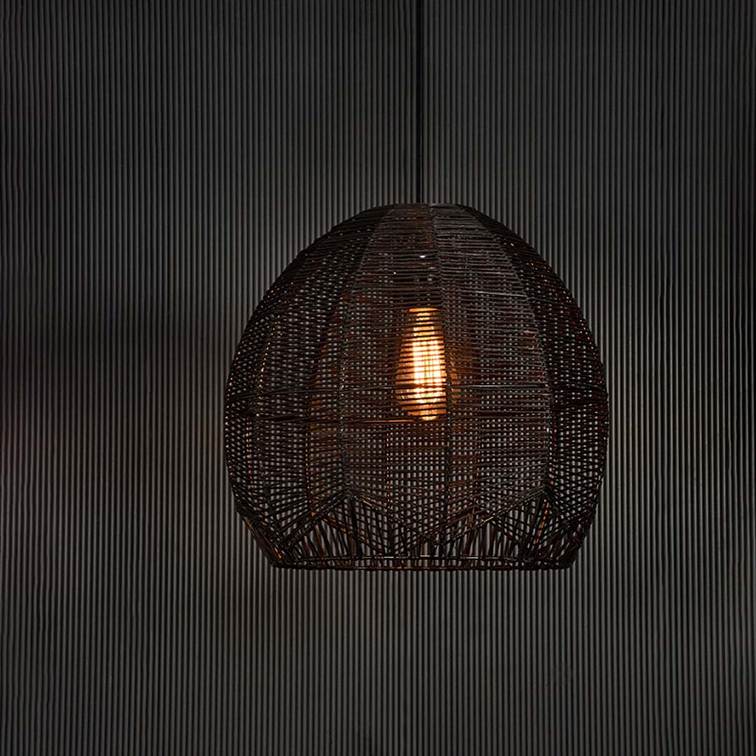 Black rattan pendant light glowing softly on dark background creating a modern and luxurious ambiance with woven texture.