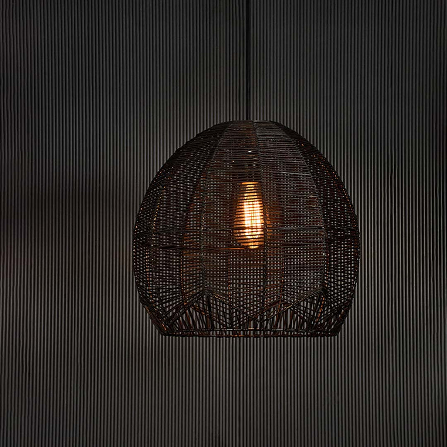 Black rattan pendant light glowing softly on dark background creating a modern and luxurious ambiance with woven texture.