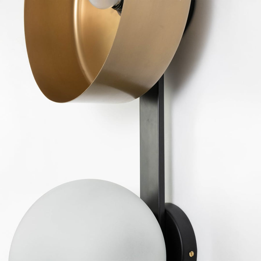 Closeup view of gold metallic bowl and frosted glass globe on black wall sconce showing material details.