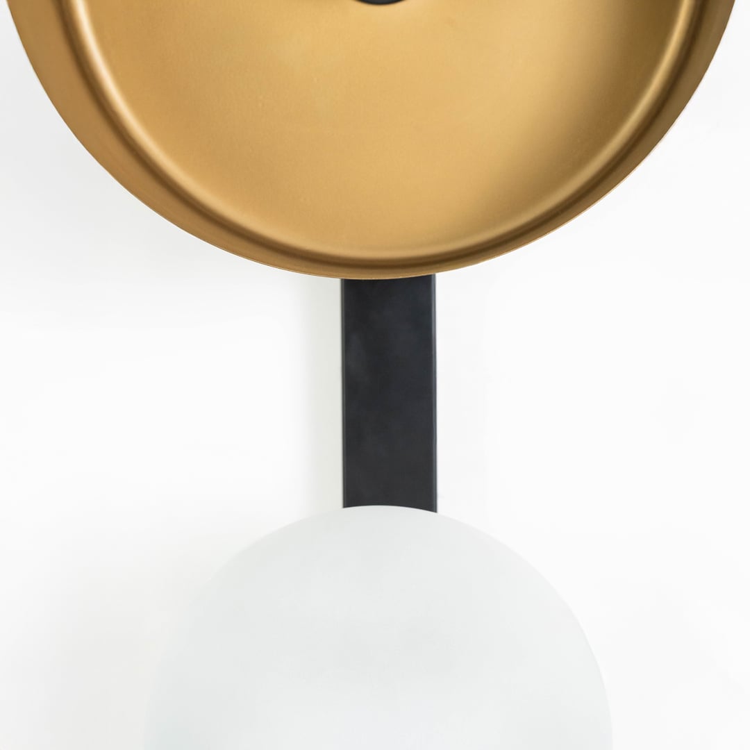 Vertical closeup of wall lamp highlighting smooth gold reflector and matte frosted glass on black base.