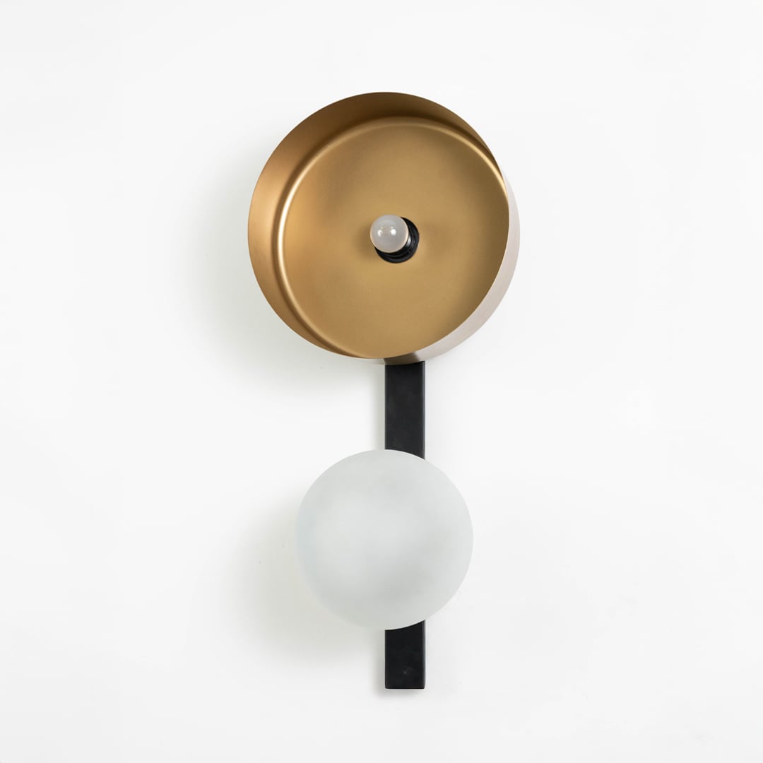 Contemporary wall sconce with gold reflector and frosted glass mounted on black strip against white background.