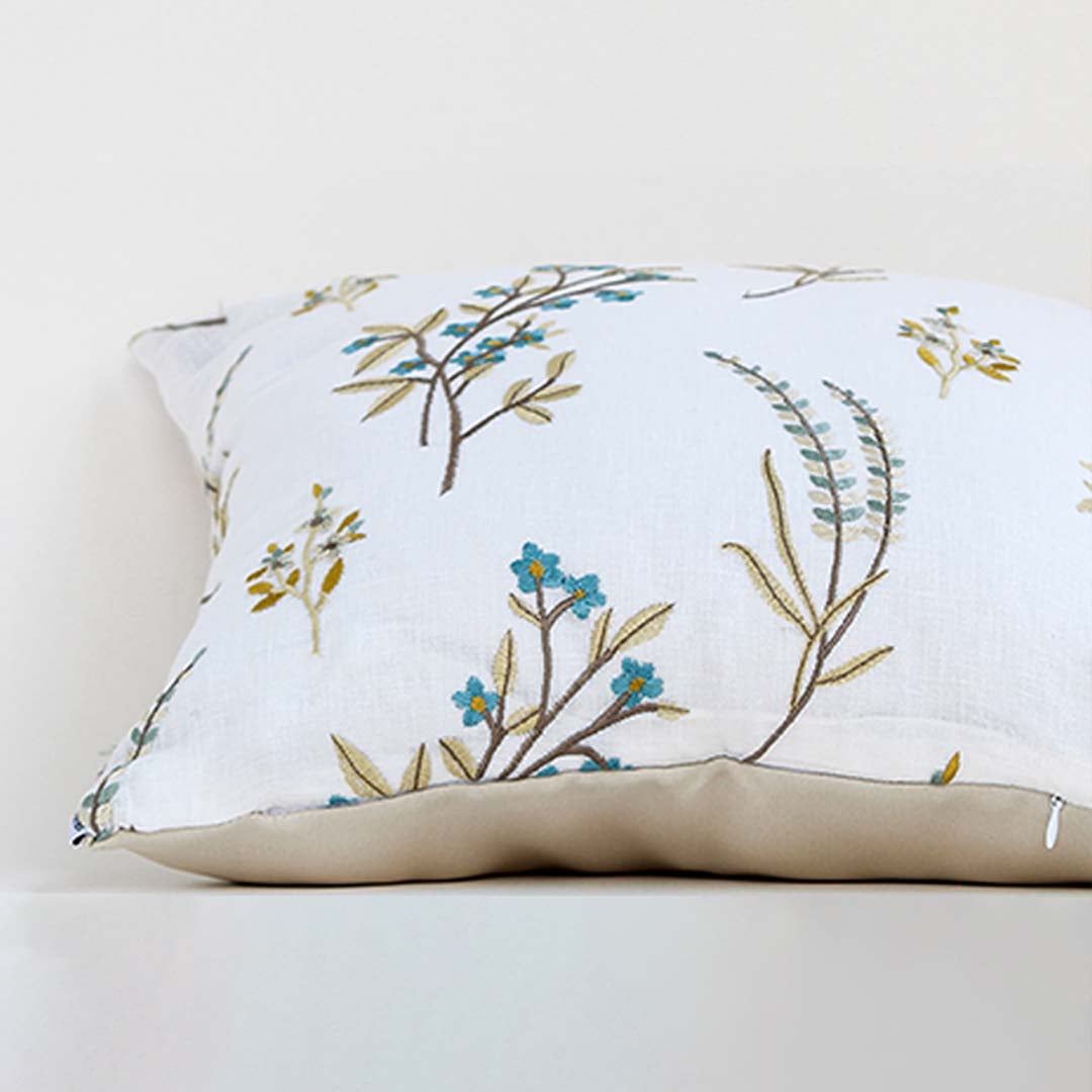 A closeup view of the embroidered floral cushion showcasing fine stitch details blue and mustard botanical motifs and fabric texture presented clearly for decorative detailing.