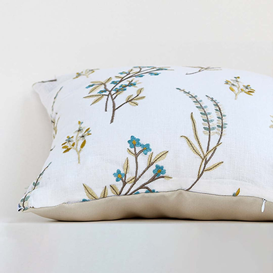 A closeup view of the embroidered floral cushion showcasing fine stitch details blue and mustard botanical motifs and fabric texture presented clearly for decorative detailing.