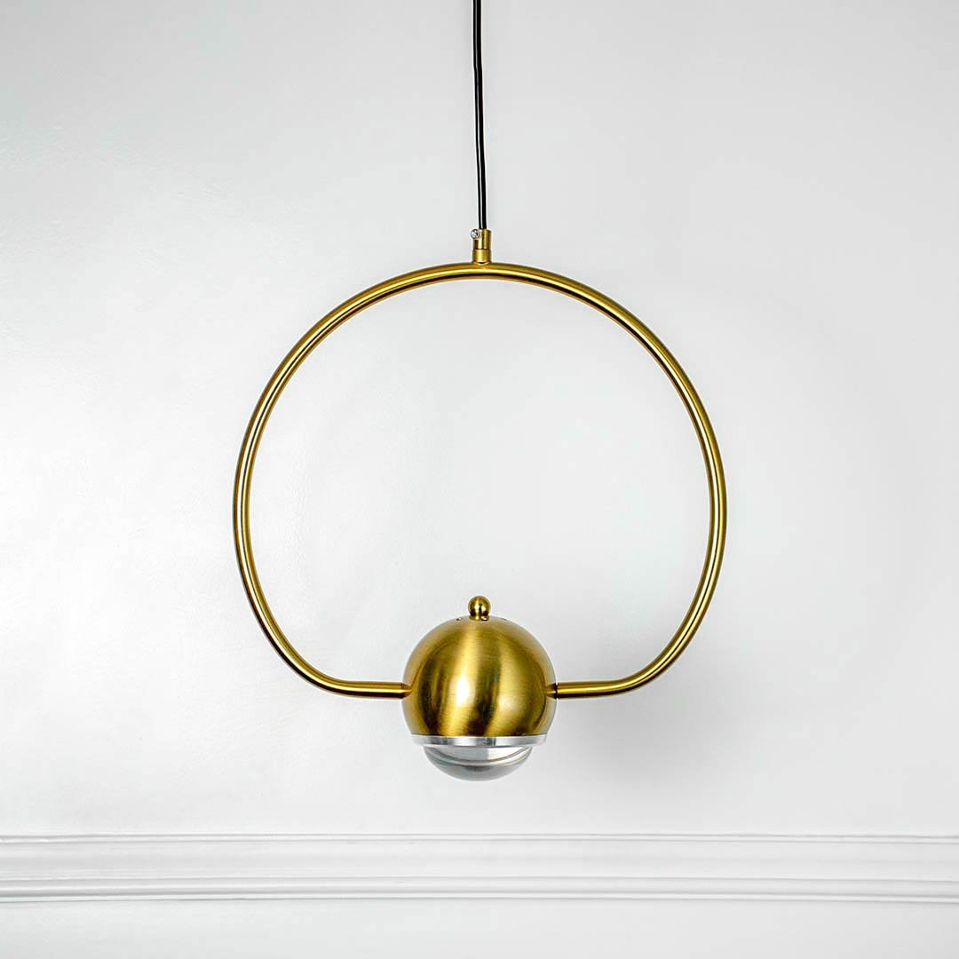 Gold circular ring pendant light with central bulb holder and hanging cord placed against neutral wall background highlighting elegant contemporary lighting design.