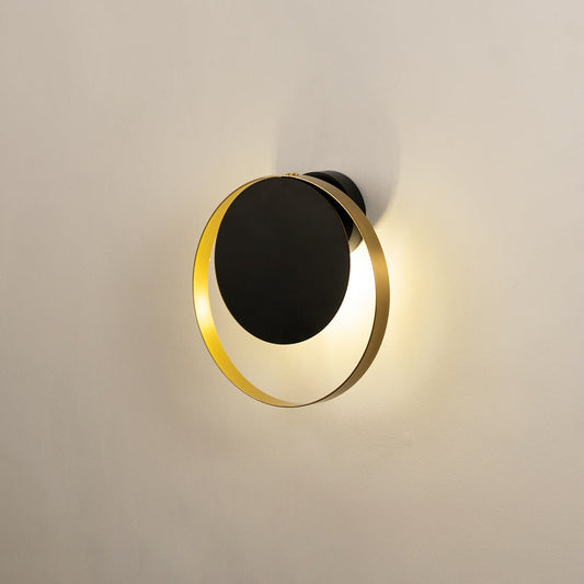 Modern black and brass wall light with warm halo glow for elegant bedroom and hallway decor.