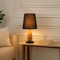 Black fabric shade table lamp with natural wood base casting warm ambient light on bedside table in cozy interiors.