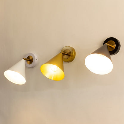 Three cone-shaped wall sconces in white gold and black finishes each lit and mounted on a light-colored wall.