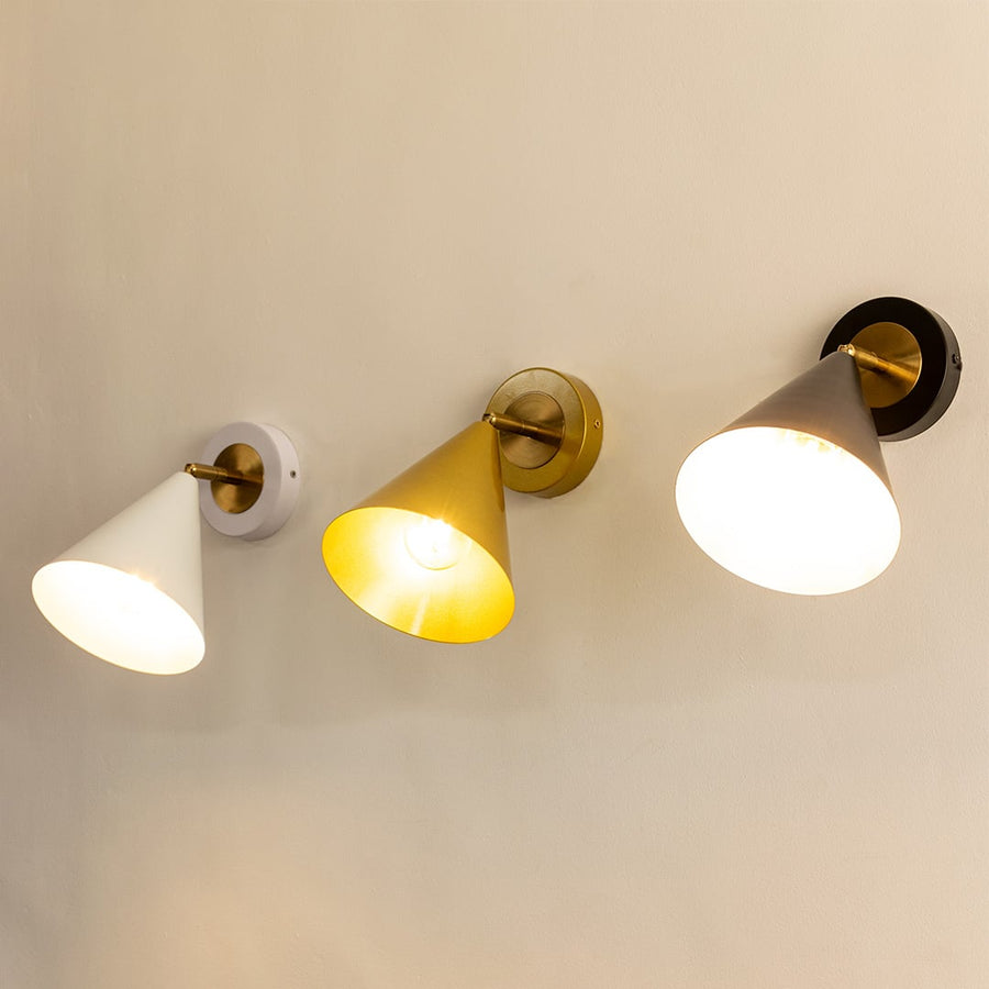 Three cone-shaped wall sconces in white gold and black finishes each lit and mounted on a light-colored wall.