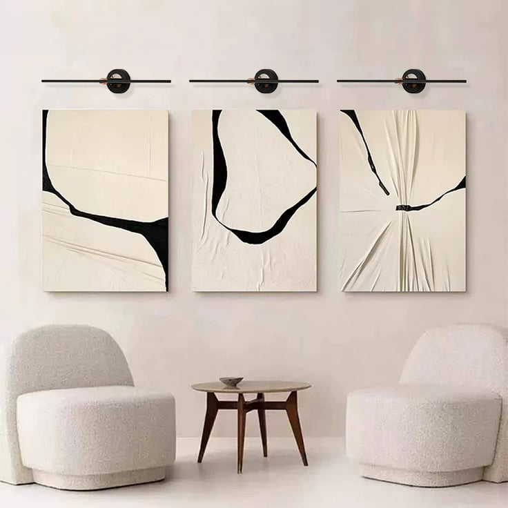Black and gold metal picture lights illuminating abstract artwork with focused lighting for contemporary living room decor.