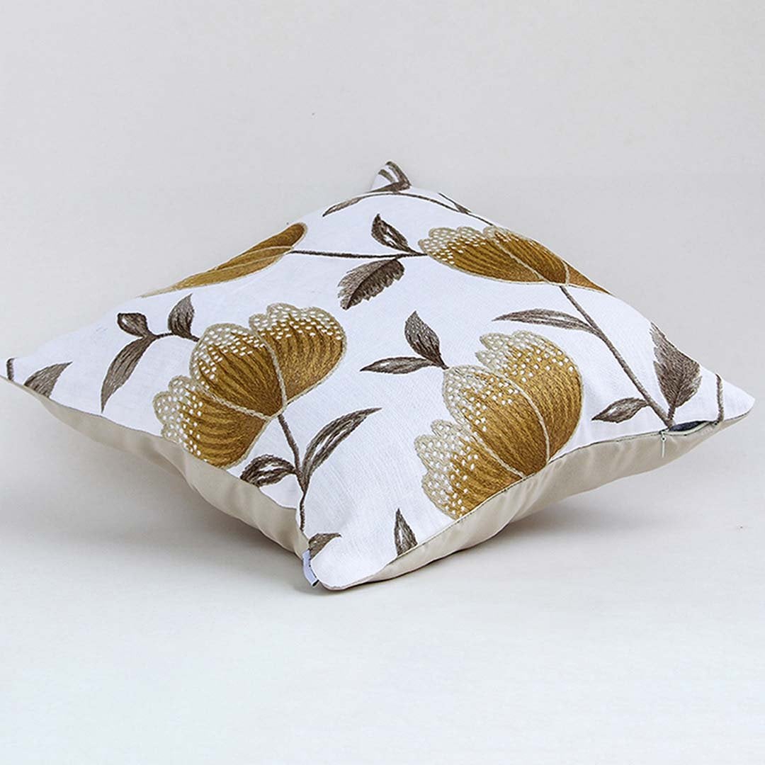 White cotton cushion cover with large golden botanical motifs shown at an angle adding a premium nature inspired décor accent with a soft breathable and skin friendly fabric.