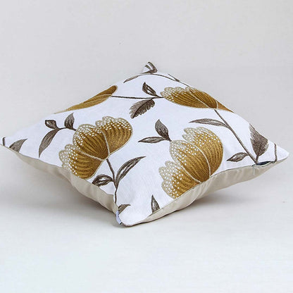 White cotton cushion cover with large golden botanical motifs shown at an angle adding a premium nature inspired décor accent with a soft breathable and skin friendly fabric.