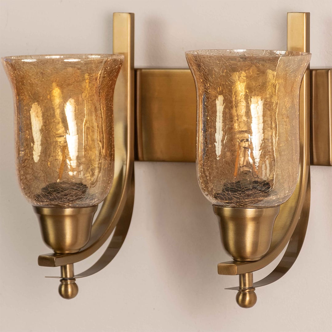 Close up view of brass double wall sconce showing curved metal arms rectangular backplates and amber crackle glass details.