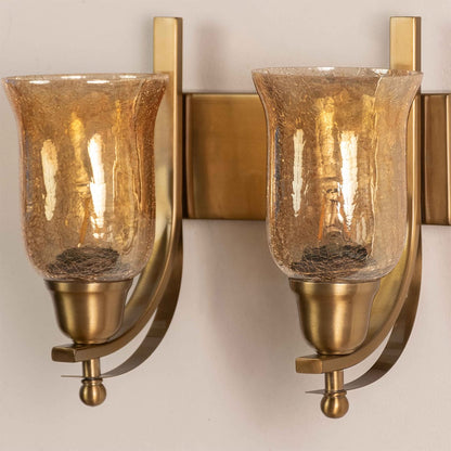 Close up view of brass double wall sconce showing curved metal arms rectangular backplates and amber crackle glass details.