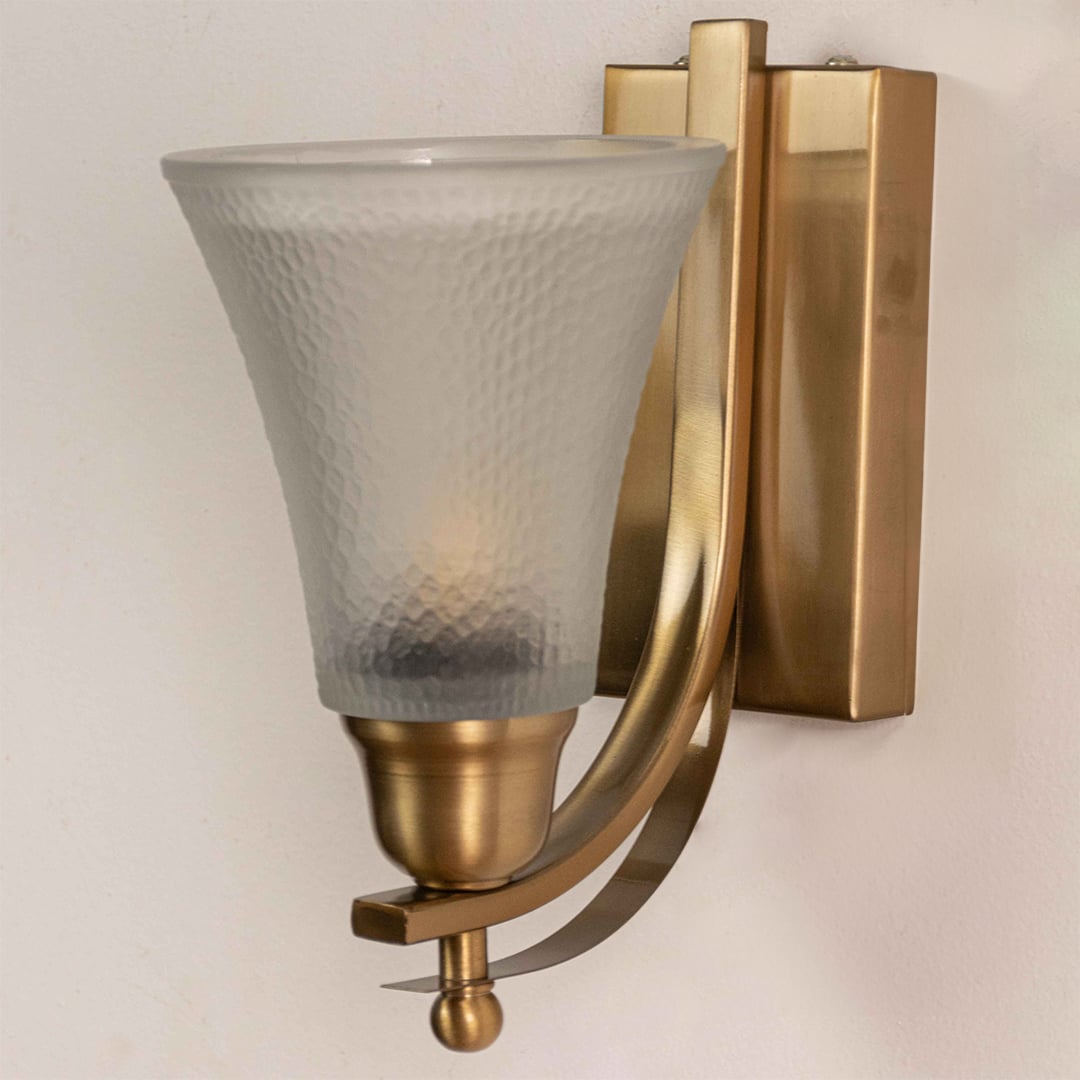 Close up view of brass wall light showing curved metal arm rectangular backplate and frosted textured glass shade details.