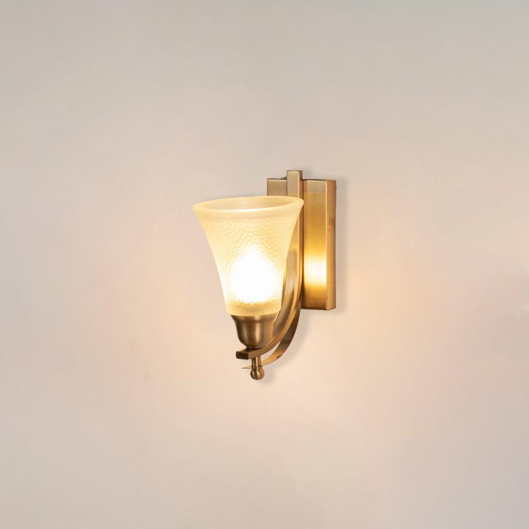 Illuminated brass wall sconce with glowing frosted glass shade and curved arm design on clean white background display.