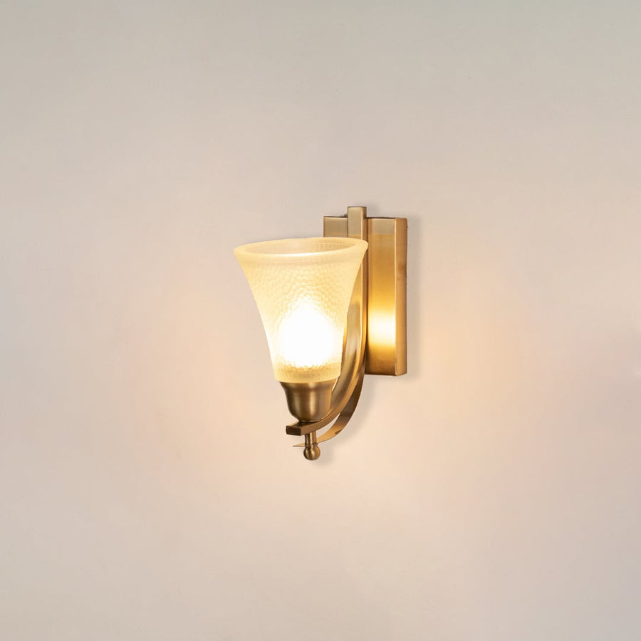 Illuminated brass wall sconce with glowing frosted glass shade and curved arm design on clean white background display.