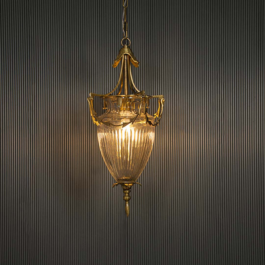 Glowing antique brass glass lantern turned on suspended against a dark black background highlighting the warm light emission.