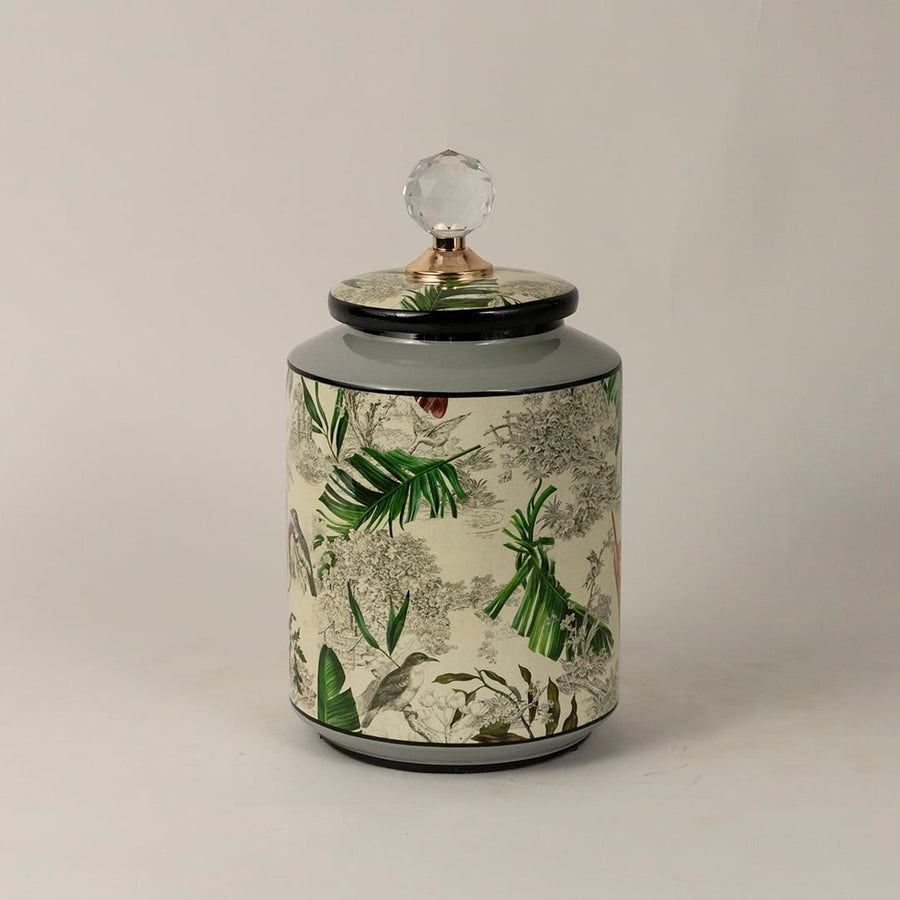 Side view of tropical bird jar highlighting cylindrical body vivid leaf artwork and shiny crystal top.