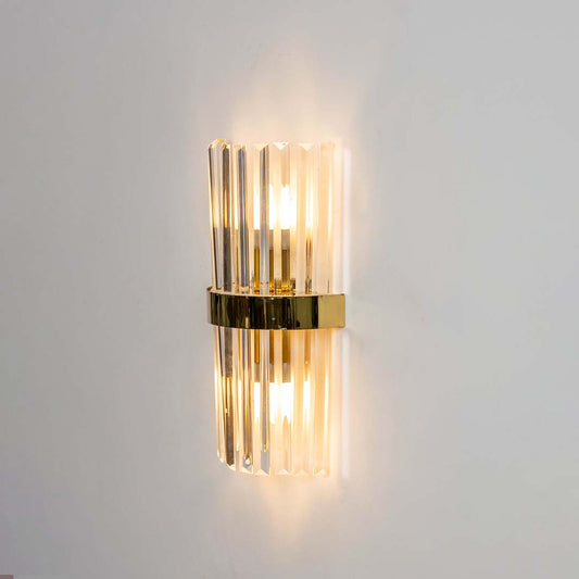 Crystal wall light shown with the light on against a white background highlighting the clear glass rods and golden band with a bright warm glow.