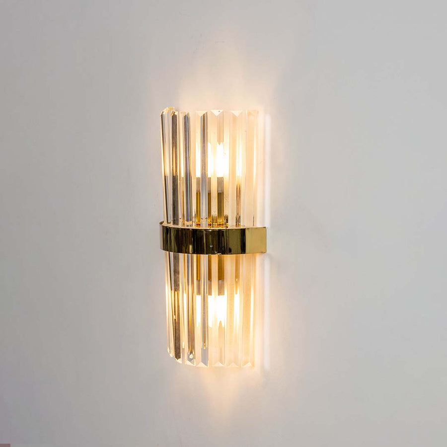 Crystal wall light shown with the light on against a white background highlighting the clear glass rods and golden band with a bright warm glow.