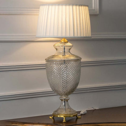 Crystal glass table lamp with brass base and pleated white shade turned on against white background perfect for bedroom or hallway illumination.