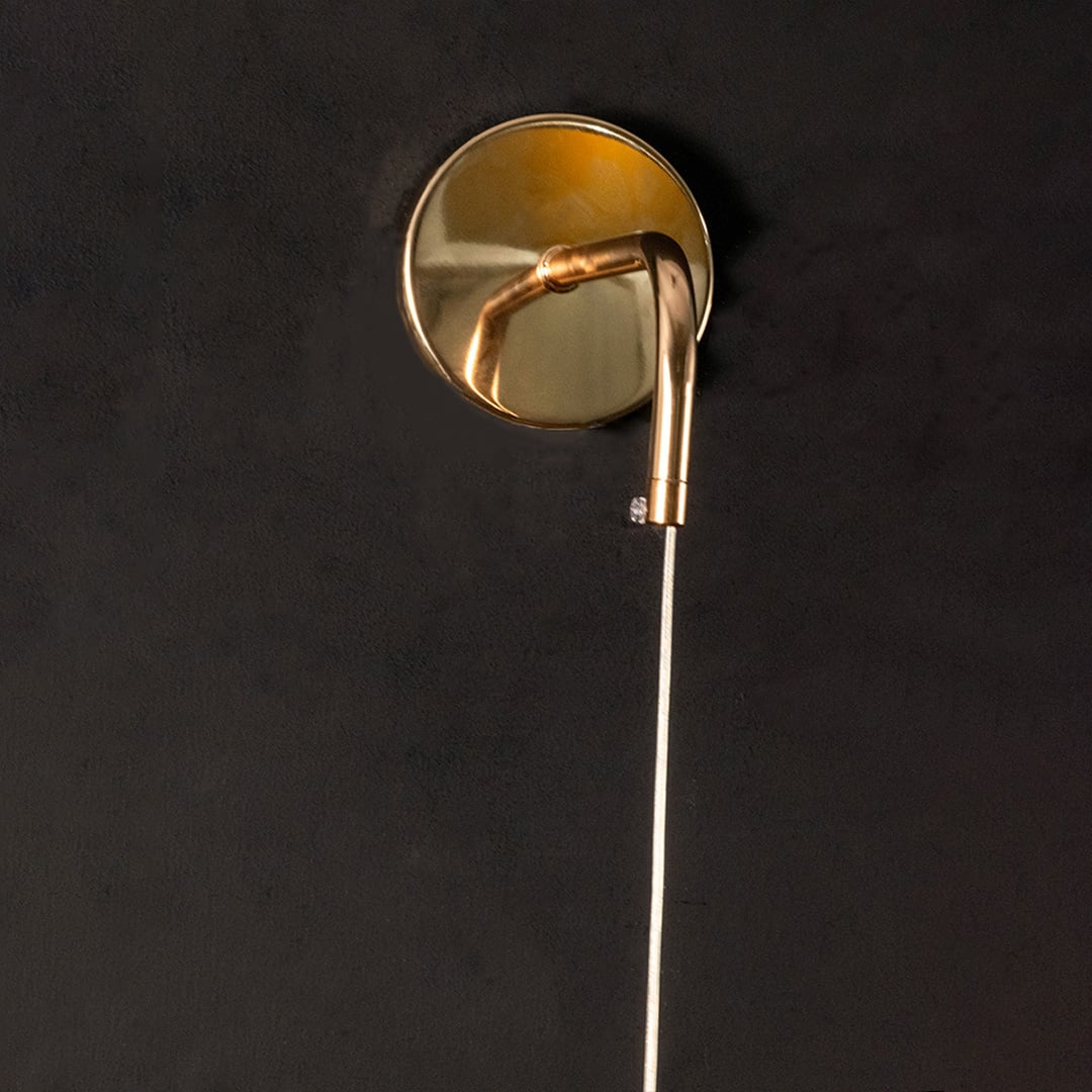 Closeup of gold metal wall light mount and curved arm highlighting smooth finish premium build and elegant lighting craftsmanship.