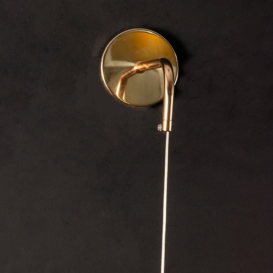 Closeup of gold metal wall light mount and curved arm highlighting smooth finish premium build and elegant lighting craftsmanship.