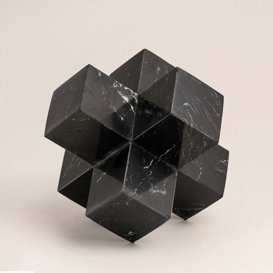 Black marble geometric sculpture with sharp angles displayed on a white background highlighting its design.