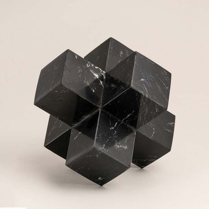 Black marble geometric sculpture with sharp angles displayed on a white background highlighting its design.