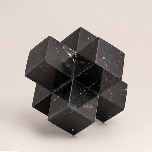 Black marble geometric sculpture with sharp angles displayed on a white background highlighting its design.
