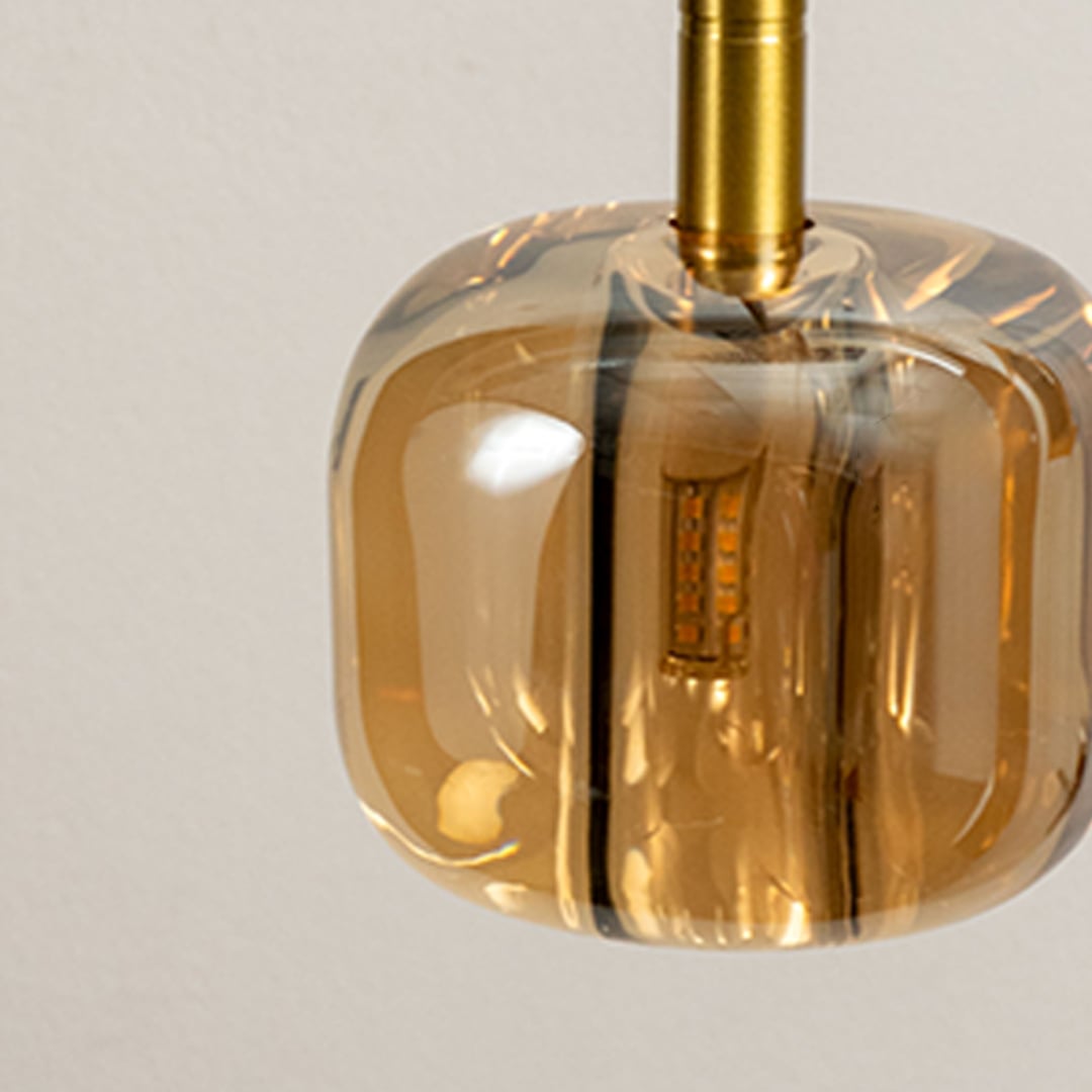 Close up of an amber glass pendant light with gold accents focusing on its sleek contemporary design and exposed light bulb.