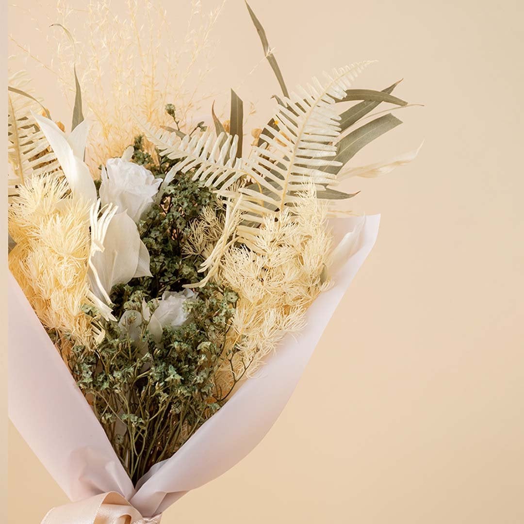 Closeup of preserved white infinity rose bouquet featuring eucalyptus miscanthus grass and fern leaves.