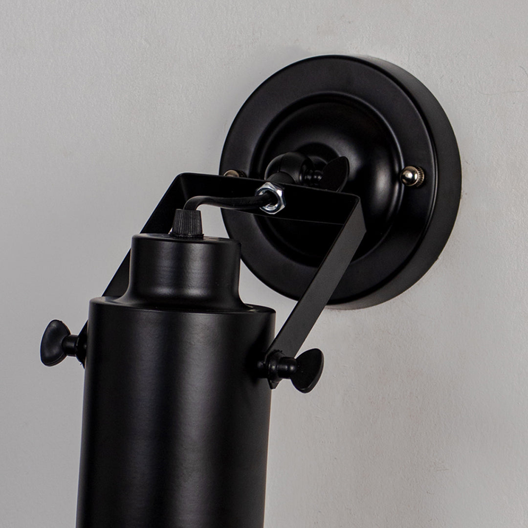 Adjustable black metal wall light with cylindrical shade and wall mount on neutral background modern task lighting for interior decor.

