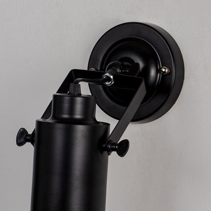 Adjustable black metal wall light with cylindrical shade and wall mount on neutral background modern task lighting for interior decor.

