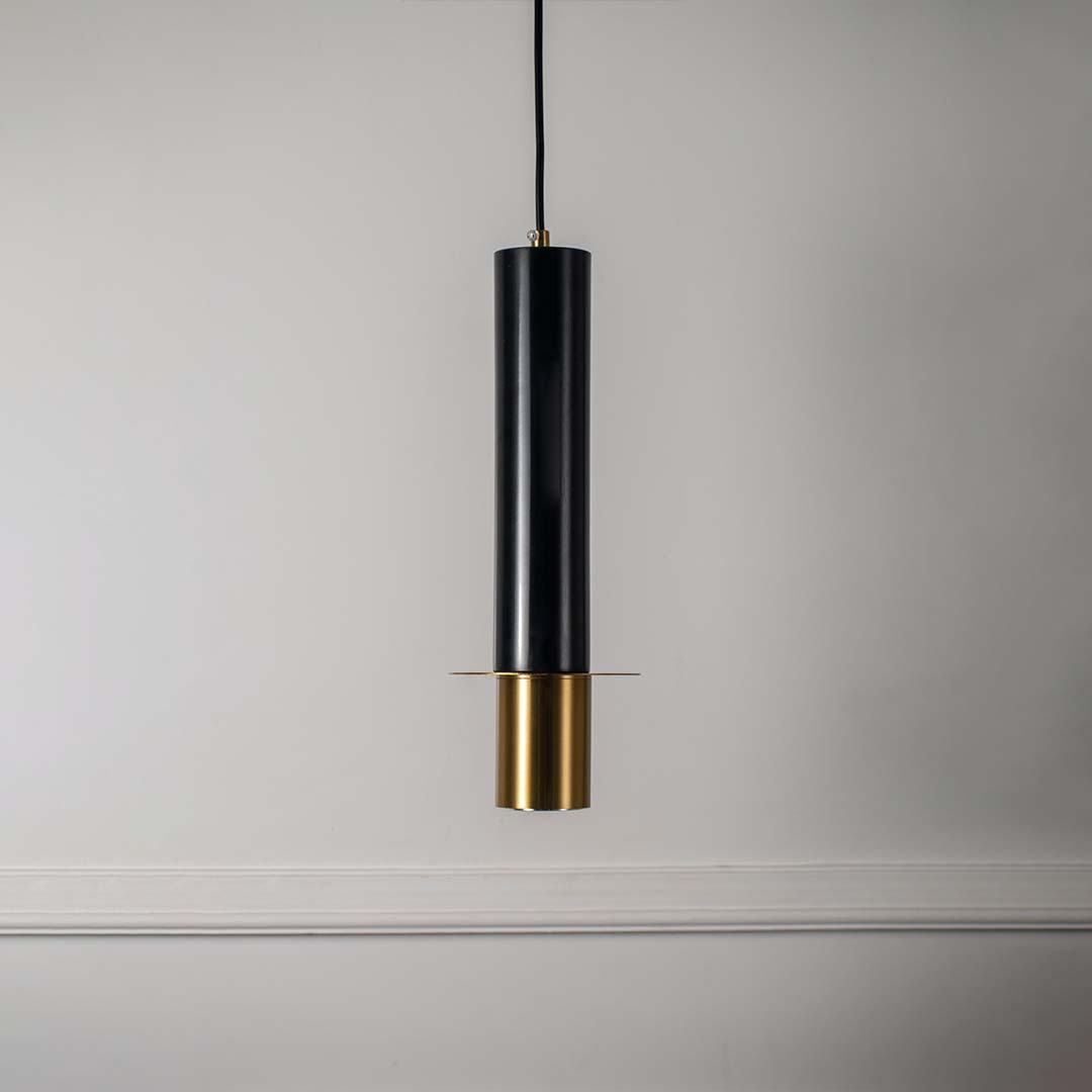 Contemporary black and gold pendant light with cylindrical shape featured against minimal off white background for style.