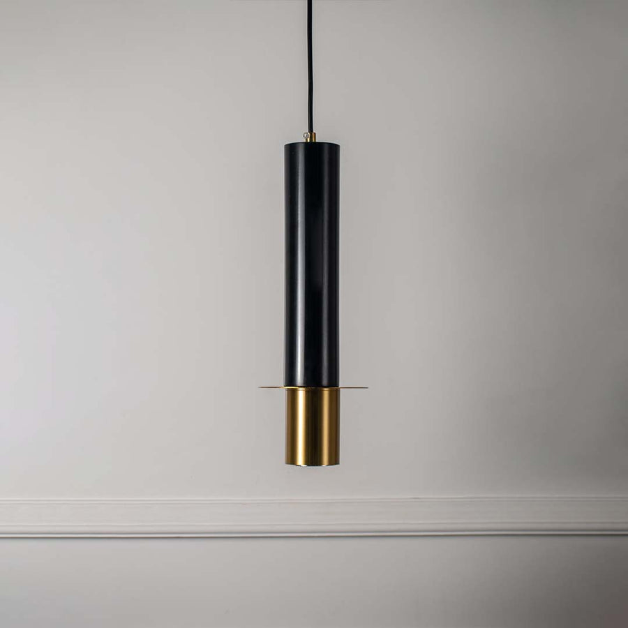 Contemporary black and gold pendant light with cylindrical shape featured against minimal off white background for style.