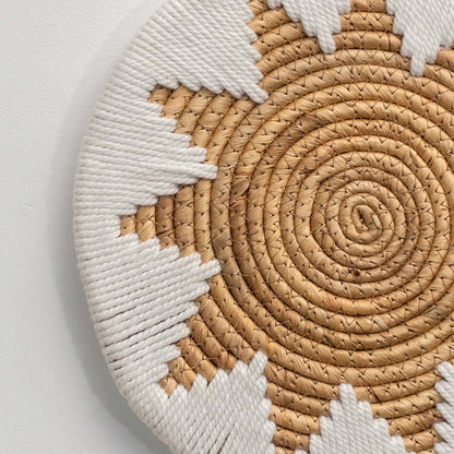 A closeup view of a beige and white woven jute wall plate revealing intricate sunburst weaving and detailed natural fiber texture.