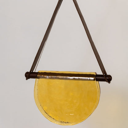 Closeup view of the pendant light highlighting the textured yellow half-moon glass shade and brown metal frame with fine detailing.