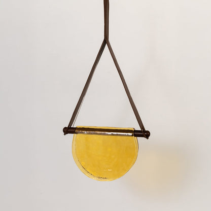 Pendant light with yellow half-moon glass shade shown turned off on a white background displaying its elegant warm-toned design.