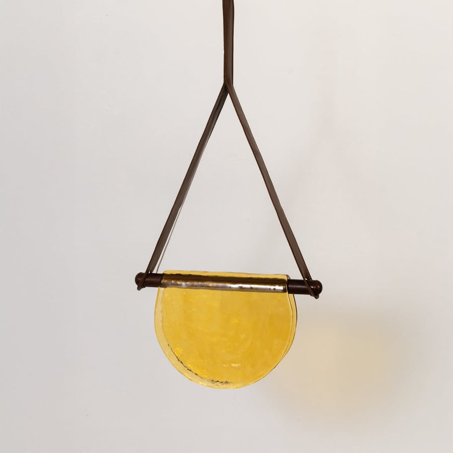 Pendant light with yellow half-moon glass shade shown turned off on a white background displaying its elegant warm-toned design.